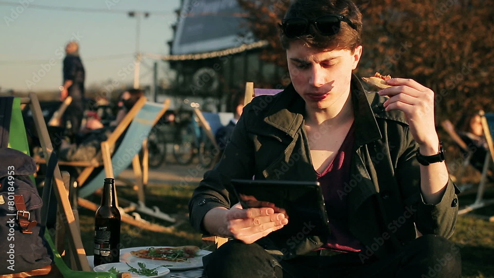 Student eating pizza and using tablet in outdoor bar