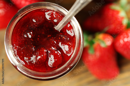 Jar of strawberry jam with berries on table close up