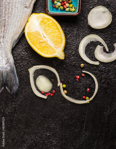Raw fish tail with lemon and spices on dark background
