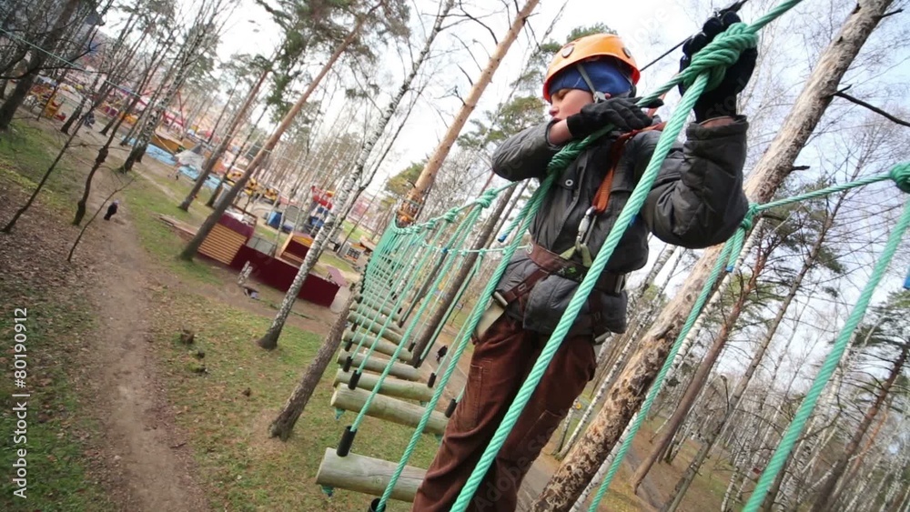 Boy stands at swinging rope way and looks down among trees Boy stands at swinging rope way and looks down among trees