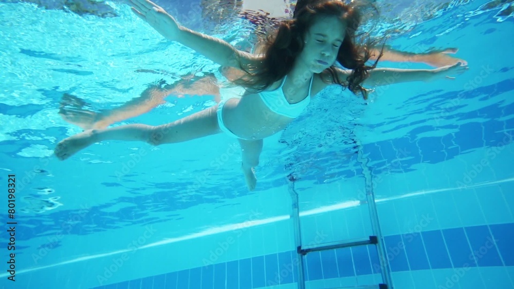 Little girl floating in blue pool face down, view under water