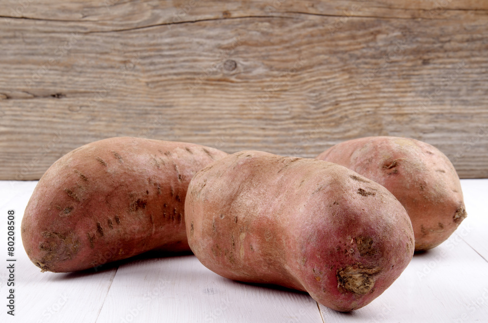 raw organic sweet potato on white wood raw organic sweet potato on white wood