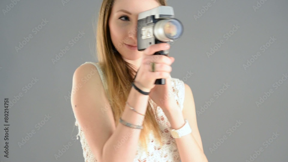 Woman with vintage camera filming against grey background. 