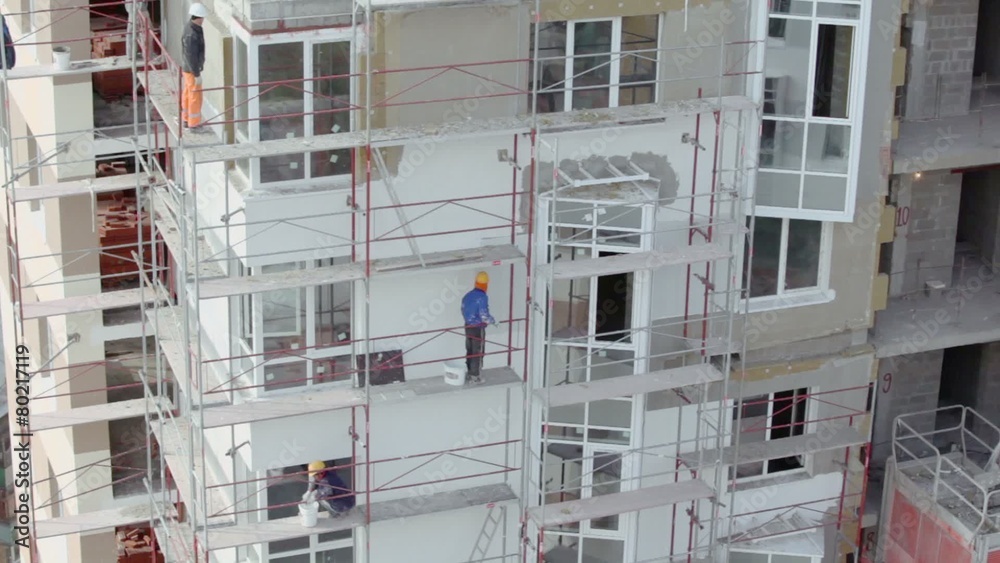 Builders stand on scaffold and make thermoinsulation of walls