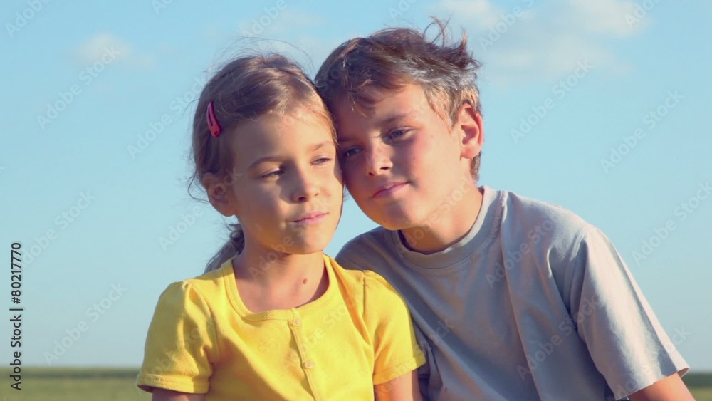 Children boy and little girl sit close together on grass hill, closeup view at sunny summer day Children boy and little girl sit close together on grass hill, closeup view at sunny summer day