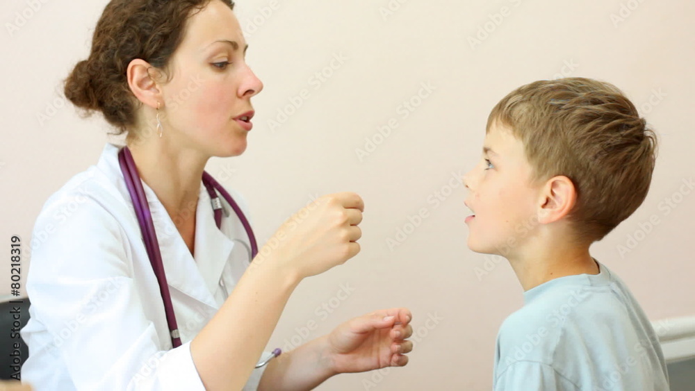 female doctor examines tongue and eyes of little boy in office female doctor examines tongue and eyes of little boy in office