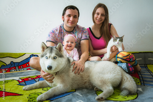 Happy young family sitting on floor with cat and dog pet at home