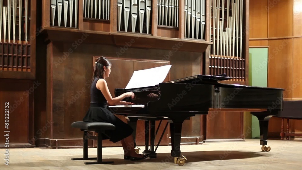 Back view woman pianist sits at the piano in concert stage
