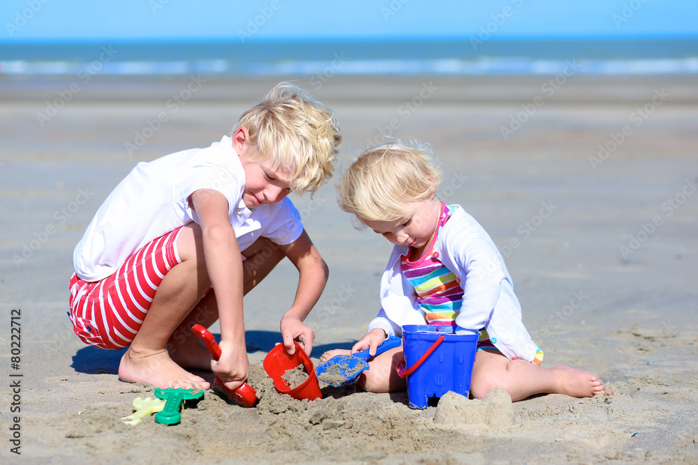Brother and sister playing with sand on the beach Brother and sister playing with sand on the beach