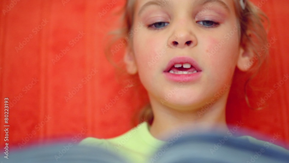 Little girl reads syllables from book aloud against red wall Little girl reads syllables from book aloud against red wall
