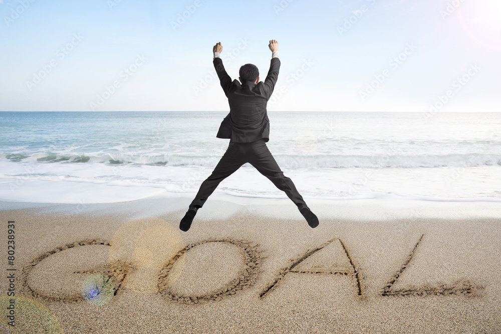 Jumping businessman cheering for goal word written on sand beach Jumping businessman cheering for goal word written on sand beach