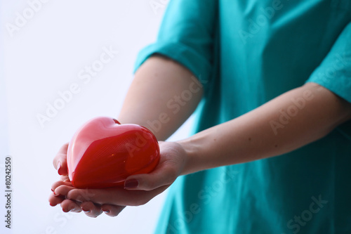 Female doctor with stethoscope holding heart over white
