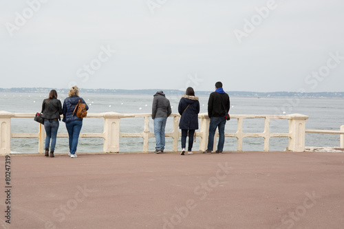 Group of friends on the pier looking in the distance the sea