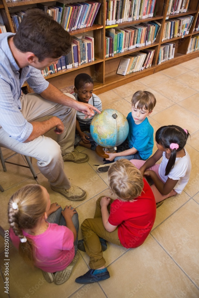 Fototapeta premium Cute pupils and teacher looking at globe in library