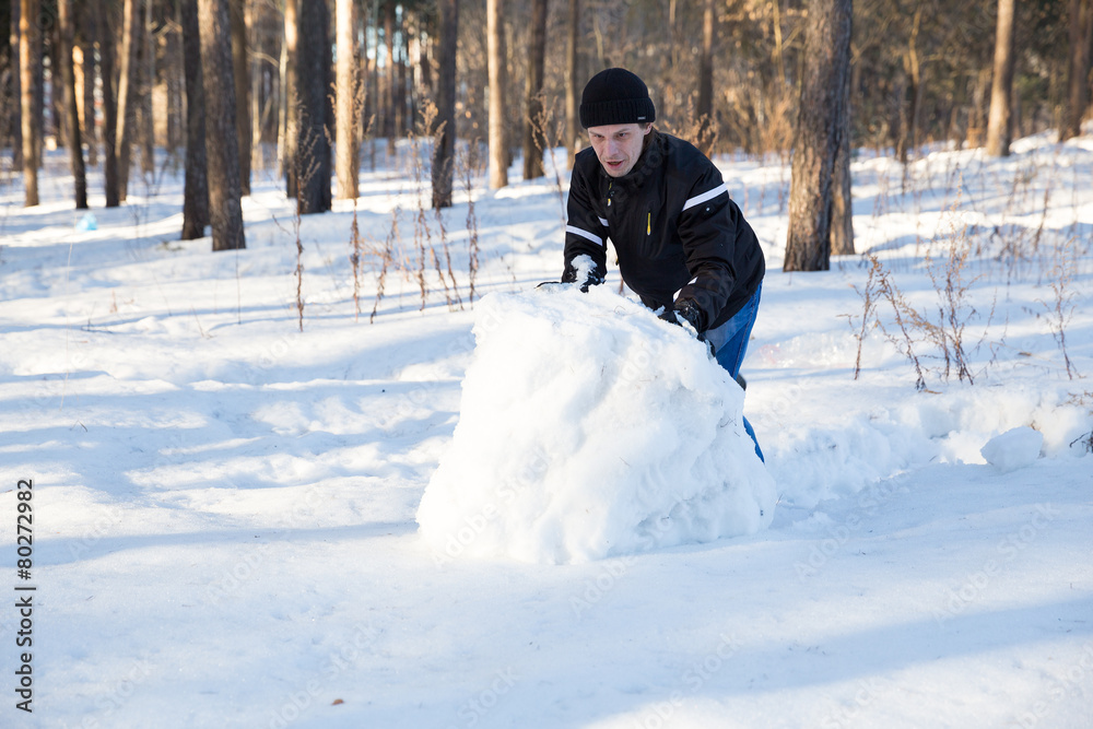 man rolls large snow globe for snowman