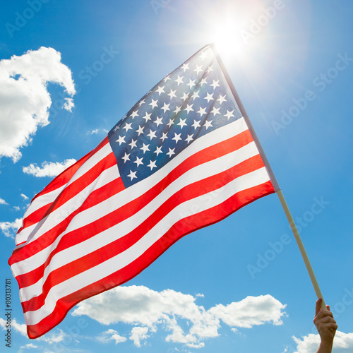 American flag waving in blue sky with sun behind it