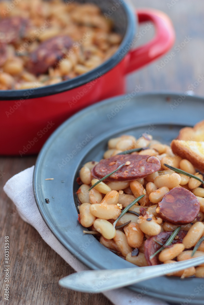 Beans and chorizo cooked with rosemary leaves on a tin plate. Beans and chorizo cooked with rosemary leaves on a tin plate.
