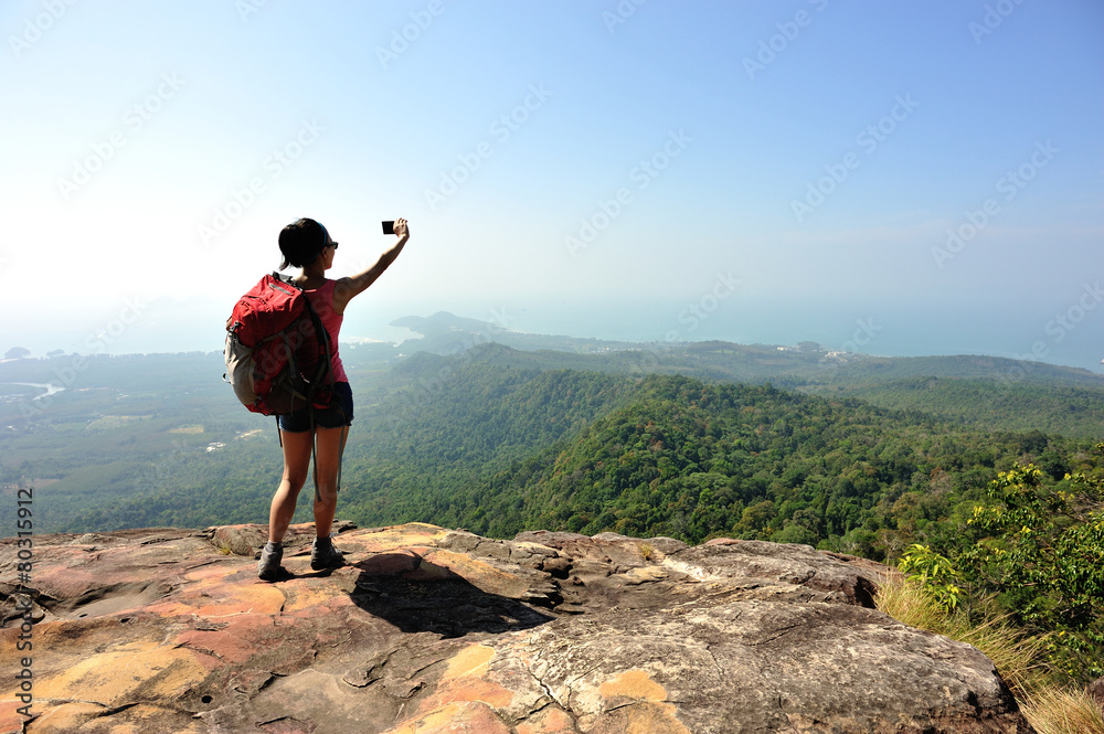 woman hiker taking photo at mountain peak cliff woman hiker taking photo at mountain peak cliff
