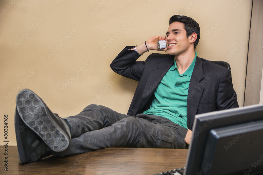 Smiling handsome young businessman at desk on phone