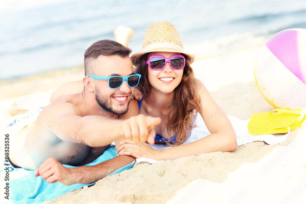 Happy couple pointing at something at the beach Happy couple pointing at something at the beach