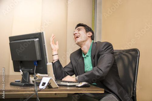 Young businessman sitting at his desk laughing
