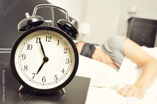 alarm clock and young man sleeping in bed with a sleep mask photo