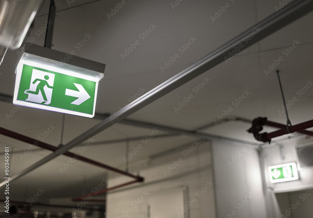 indication of the way to the emergency exit in a parking garage - obrazy, fototapety, plakaty 