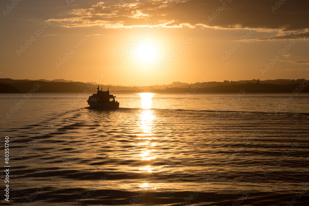 A boat departing from the harbor at sunset