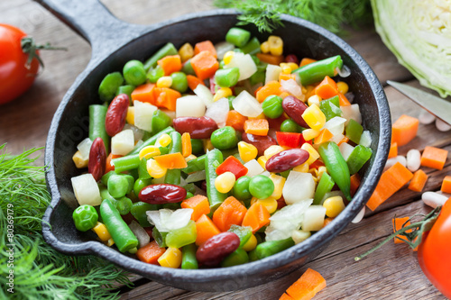 Mixed vegetables in retro frying pan and ingredients on wooden r