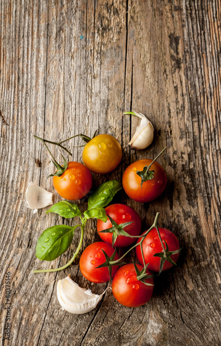 Cherry tomatoes, garlic and fresh basil on vintage wood table - rural still life from above. Harvest from garden. Background layout with free text space.