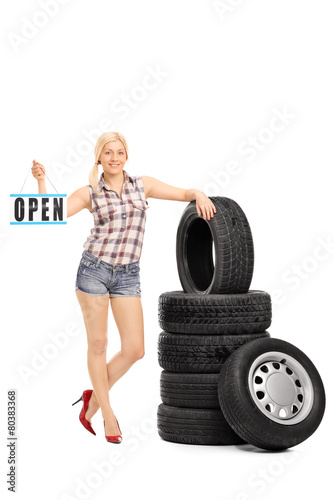 Woman holding an open sign next to a stack of tires