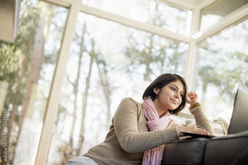 Woman sitting on the floor in front of a sofa looking at her laptop. Woman sitting on the floor in front of a sofa looking at her laptop.