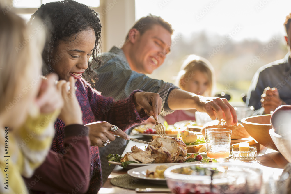 A group of people, adults and children, seated around a table for a meal. A group of people, adults and children, seated around a table for a meal.