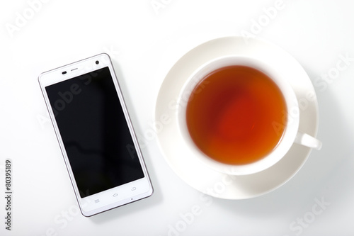 White smartphone and a cup of tea on white glass table