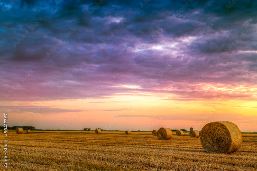 Sunset over farm field with hay bales