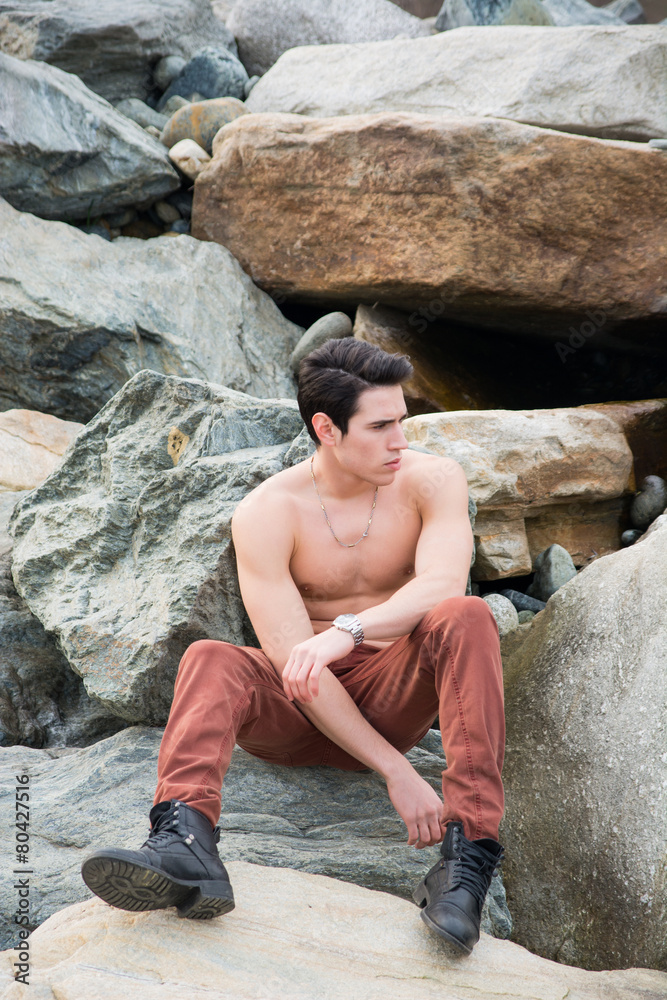 Athletic shirtless young man sitting outdoor on rocks, Athletic shirtless young man sitting outdoor on rocks,