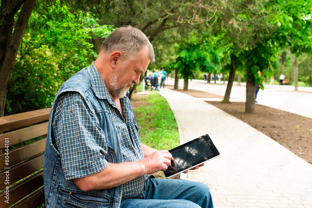 Fototapeta premium old man with tablet sitting on a bench