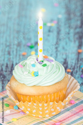 Pastel cupcake with a candle on vintage background