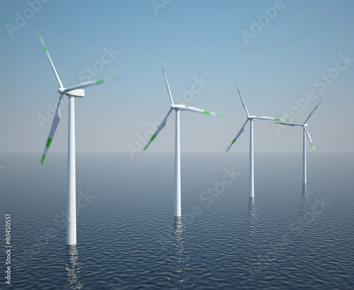 Wind turbines in motion on the ocean with blue sky.