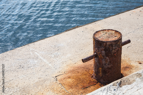 Old rusted mooring bollard on concrete pier
