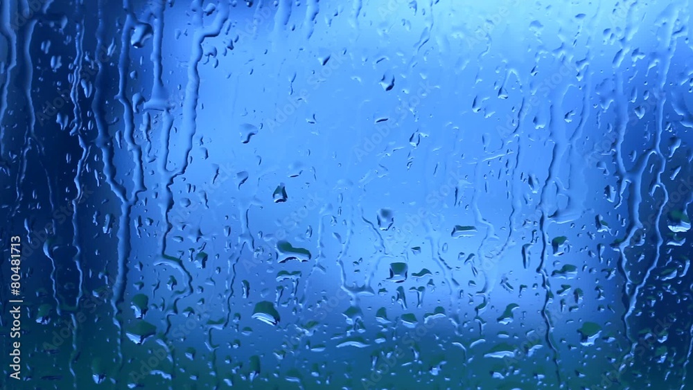 Blue color rain drops moving down a window