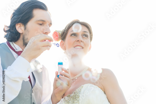 Hochzeitspaar pustet Seifenblasen auf Feld