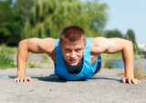Handsome young man in good shape doing push-up while outdoor tra