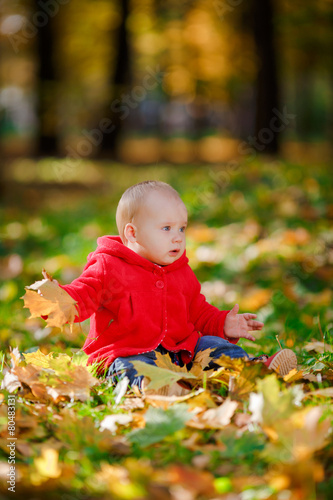 Cheerful baby in a red dress playing with yellow leaves