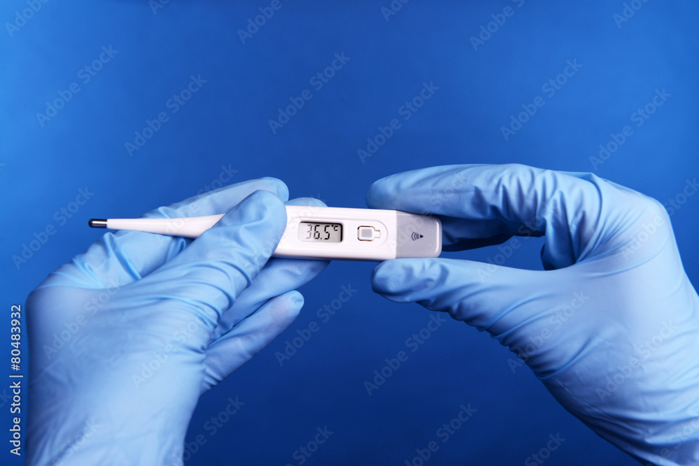 Hands with gloves holding thermometer on blue background Hands with gloves holding thermometer on blue background