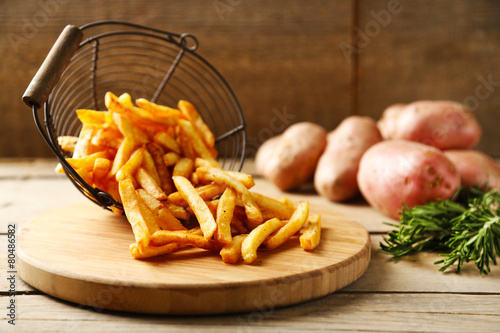Tasty french fries in metal basket on wooden table background