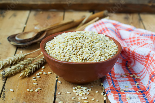 Fotografi Pearl barley in a ceramic bowl on a wooden background.selective