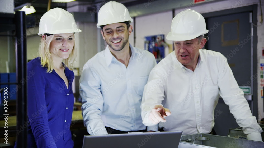 3 workers in a warehouse with a laptop are discussing their work. 3 workers in a warehouse with a laptop are discussing their work.