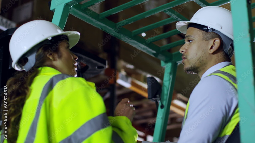 A forklift truck driver and his co-worker are working in a warehouse at night A forklift truck driver and his co-worker are working in a warehouse at night