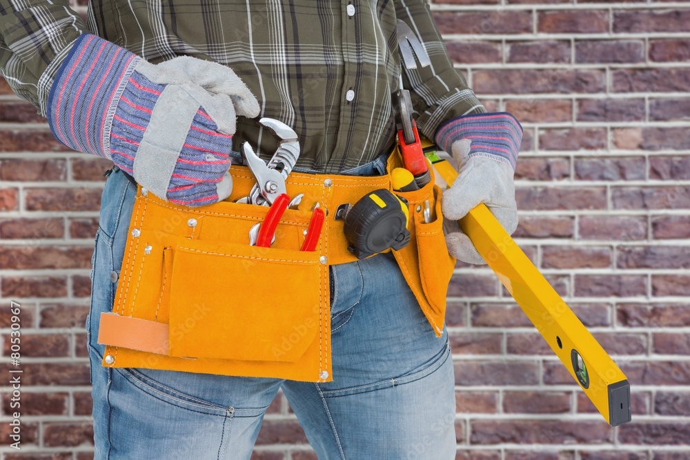 Fototapeta premium Composite image of handyman holding spirit level